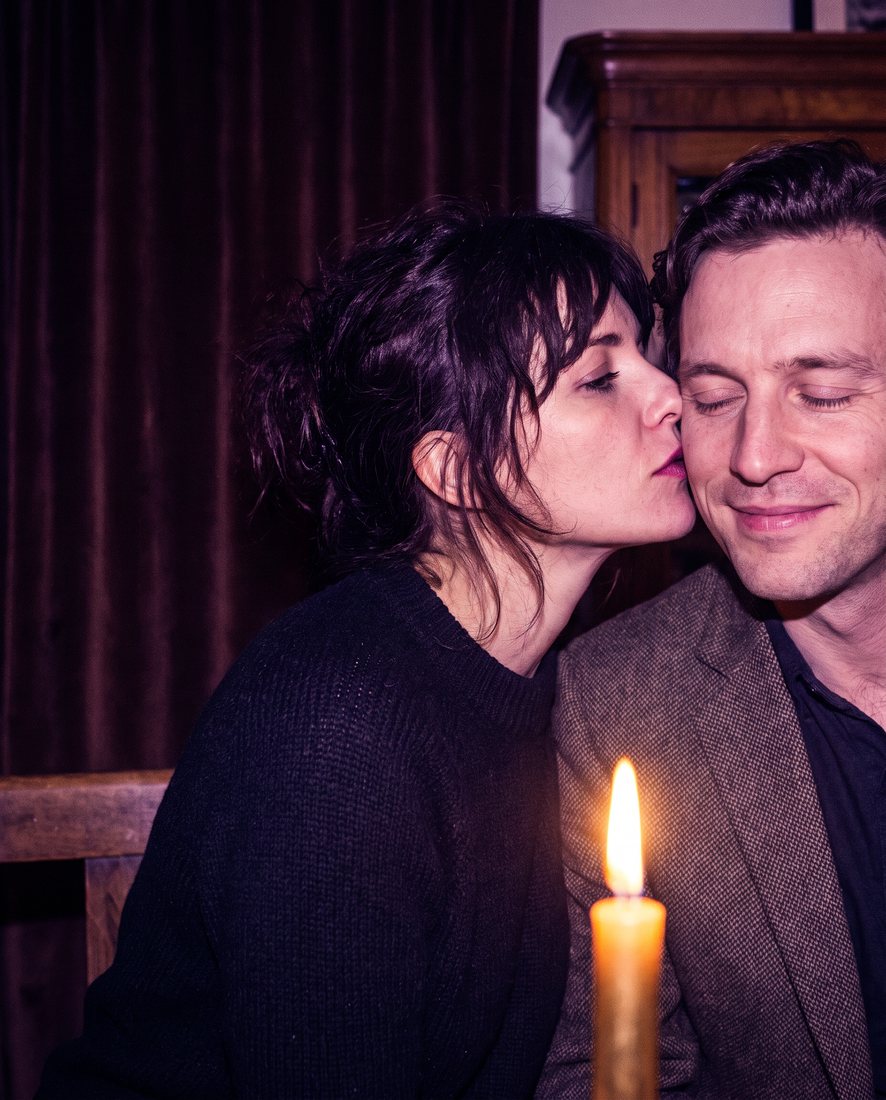 A woman kissing a smiling man on the cheek by candlelight